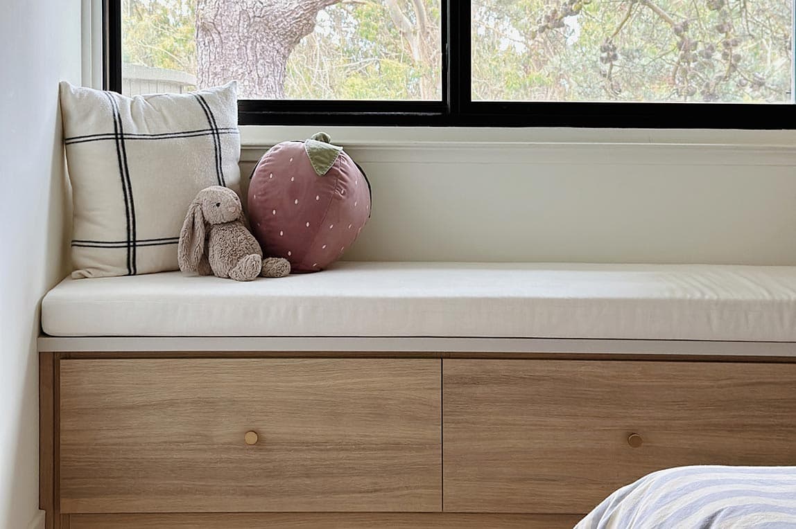 Banco de almacenamiento empotrado a medida junto a la ventana con acabado en madera clara de California Closets