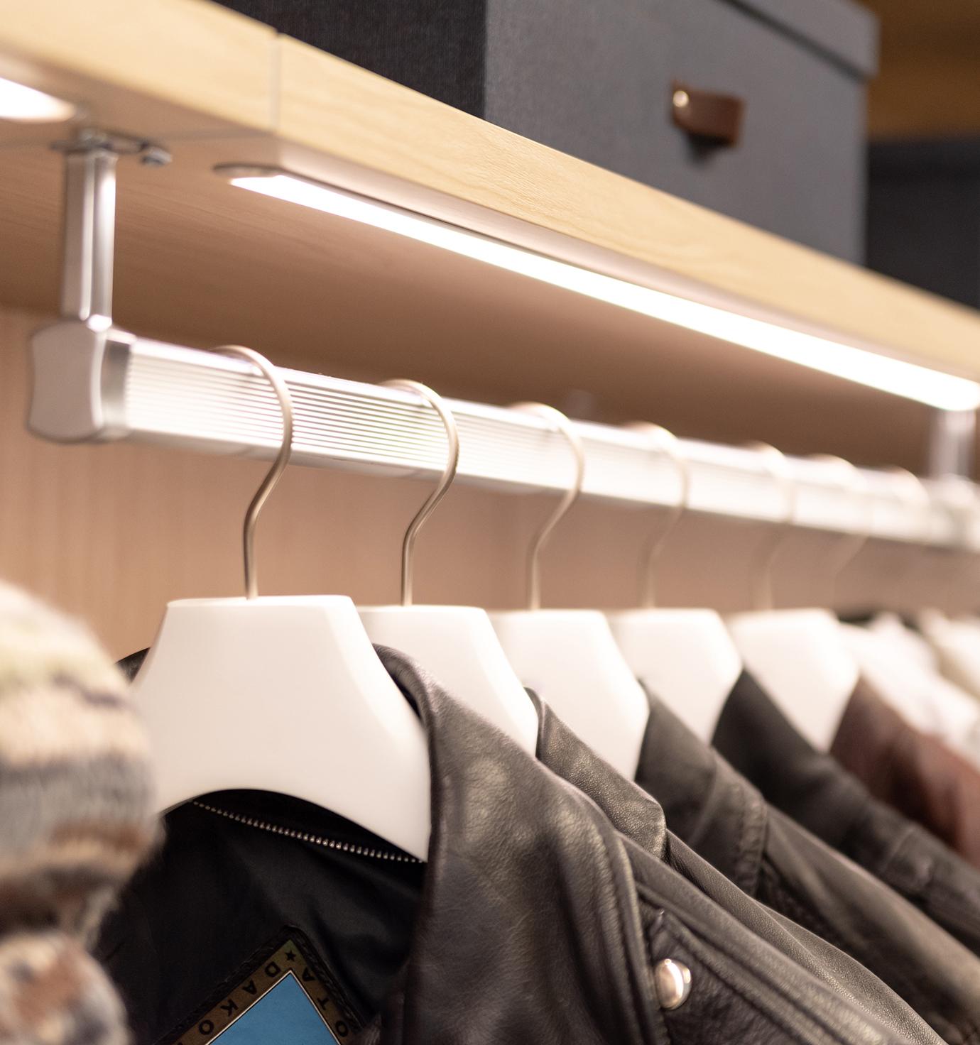 Postes de ropa iluminados en un armario con estanterías abiertas arriba de California Closets