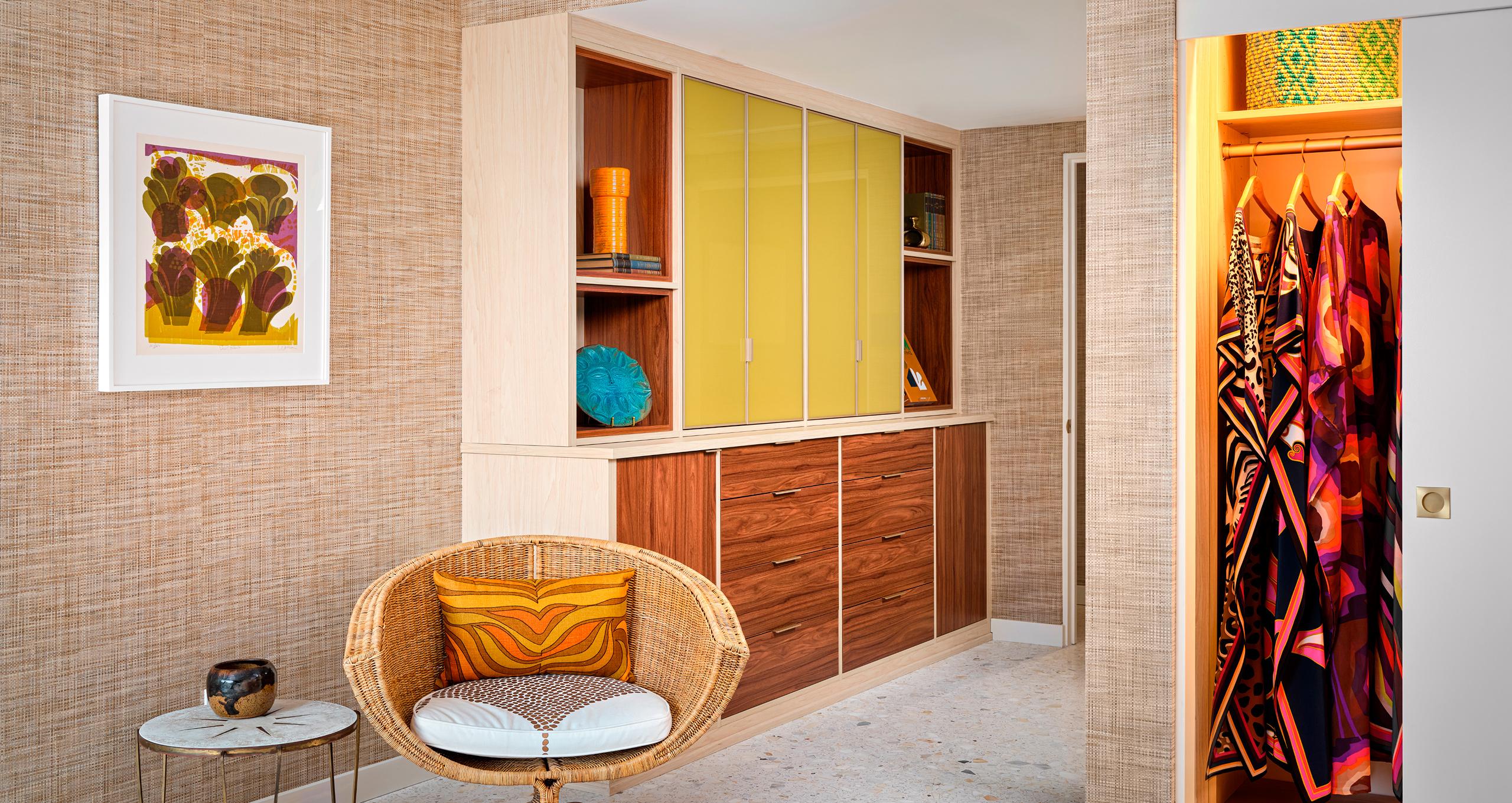 Clóset y armario modernos de mediados de siglo personalizados con puertas de vidrio amarillo, gabinetes de nogal y estantes abiertos en la casa de Trina Turk en Palm Springs, con caftanes coloridos y decoración retro.