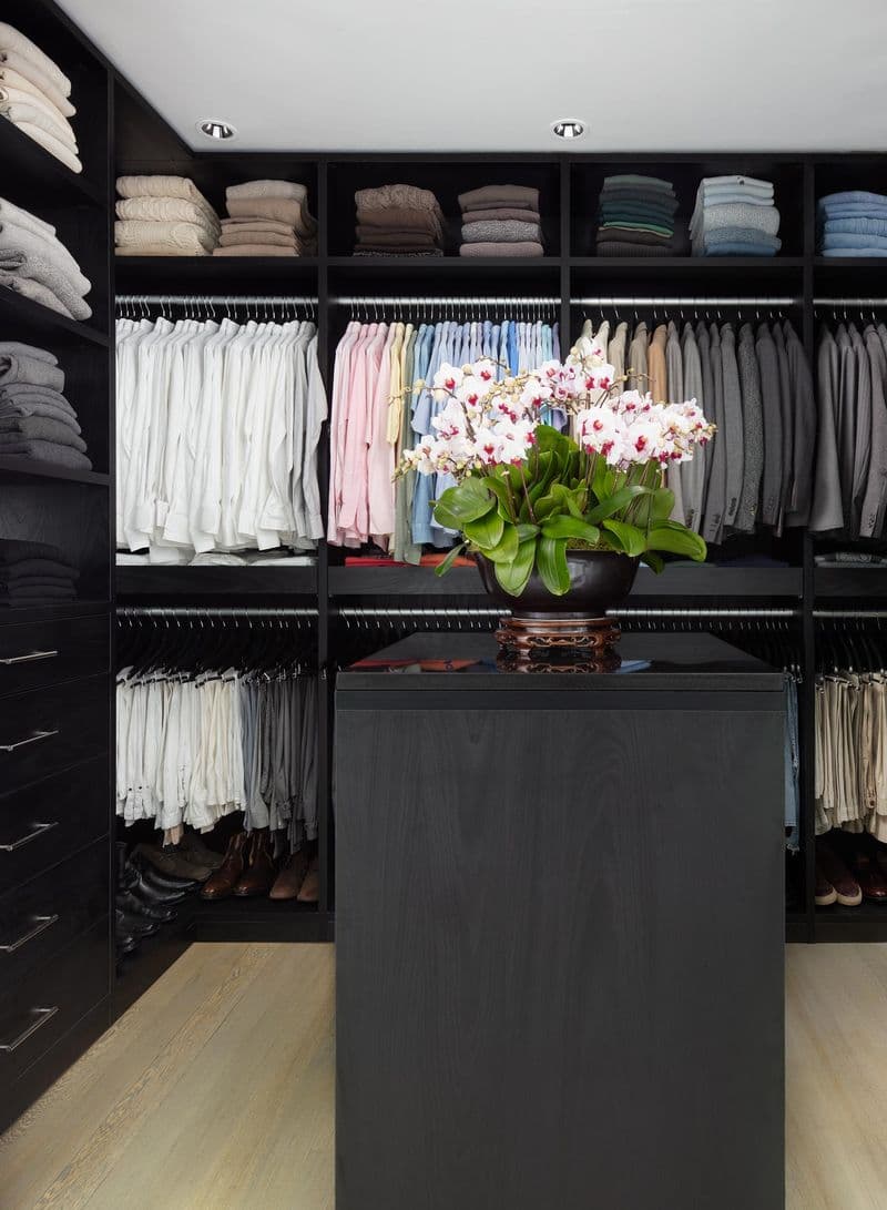 Diseño de vestidor con acabado en madera oscura y una isla central por California Closets