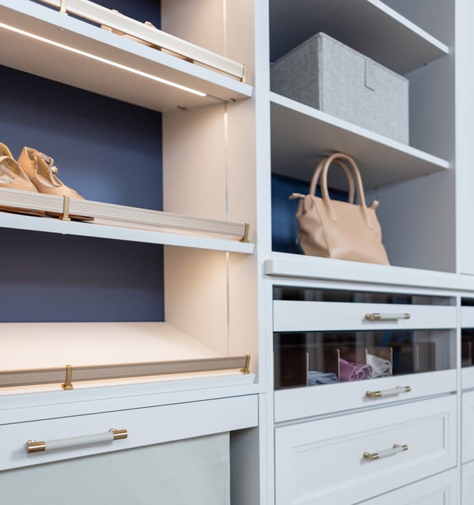 Custom closet shelving with shoe racks, guard rails, LED lighting and drawers by California Closets