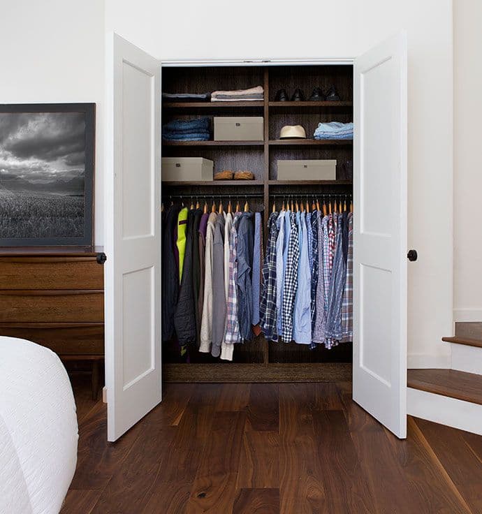 Armario empotrado para dormitorio con estantes empotrados en acabado madera oscura con puertas blancas de California Closets