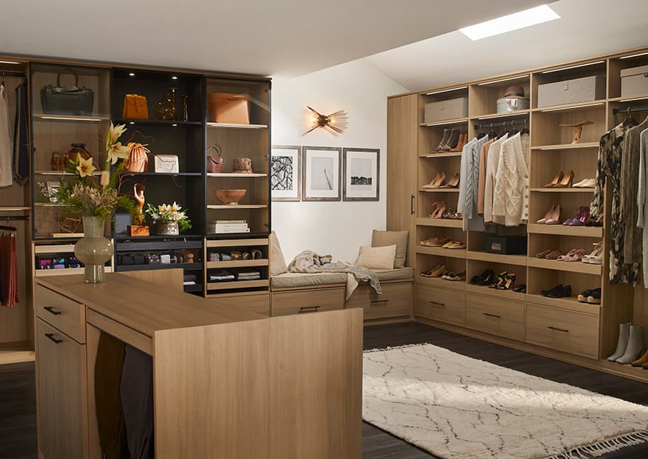 Customized walk in closet with center island and bench and with natural and LED lighting by California Closets