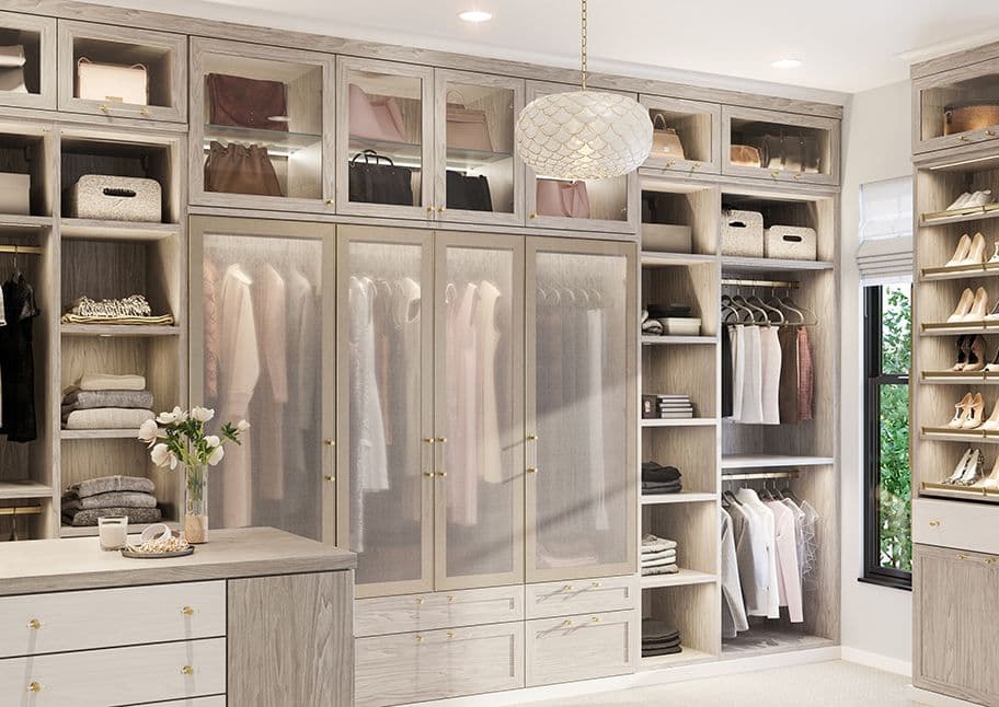 Vestidor diseñado con puertas de vidrio, tocador, isla y zapatero de California Closets.